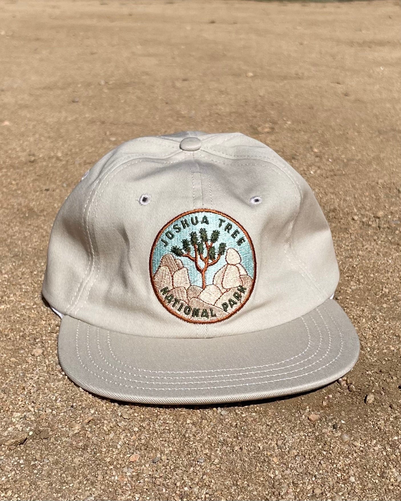 A beige baseball cap with an embroidered patch on the front displaying Joshua Tree National Park.