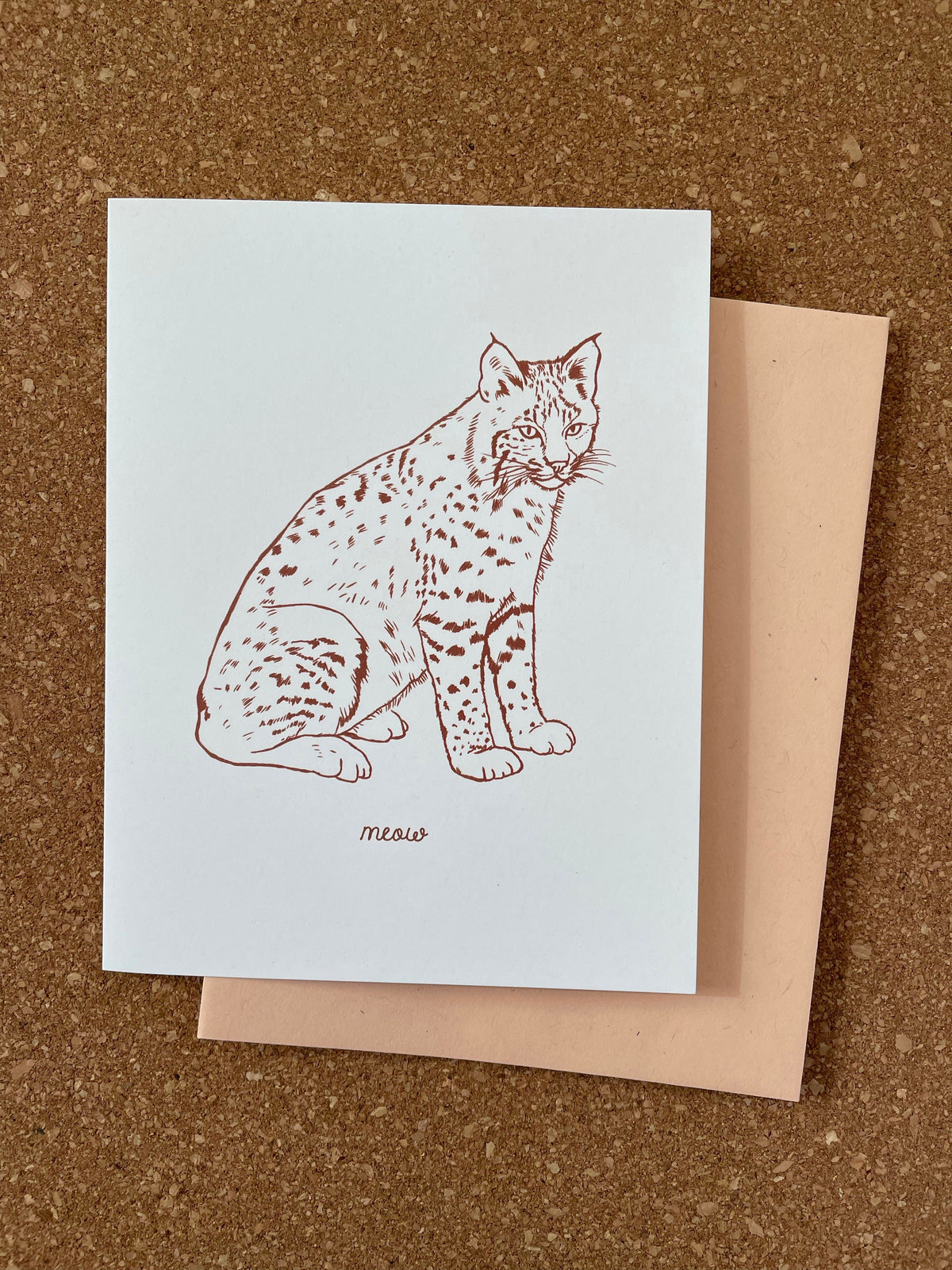 A greeting card featuring a red line drawing of a bobcat on a white background, accompanied by an orange kraft-tone envelope.