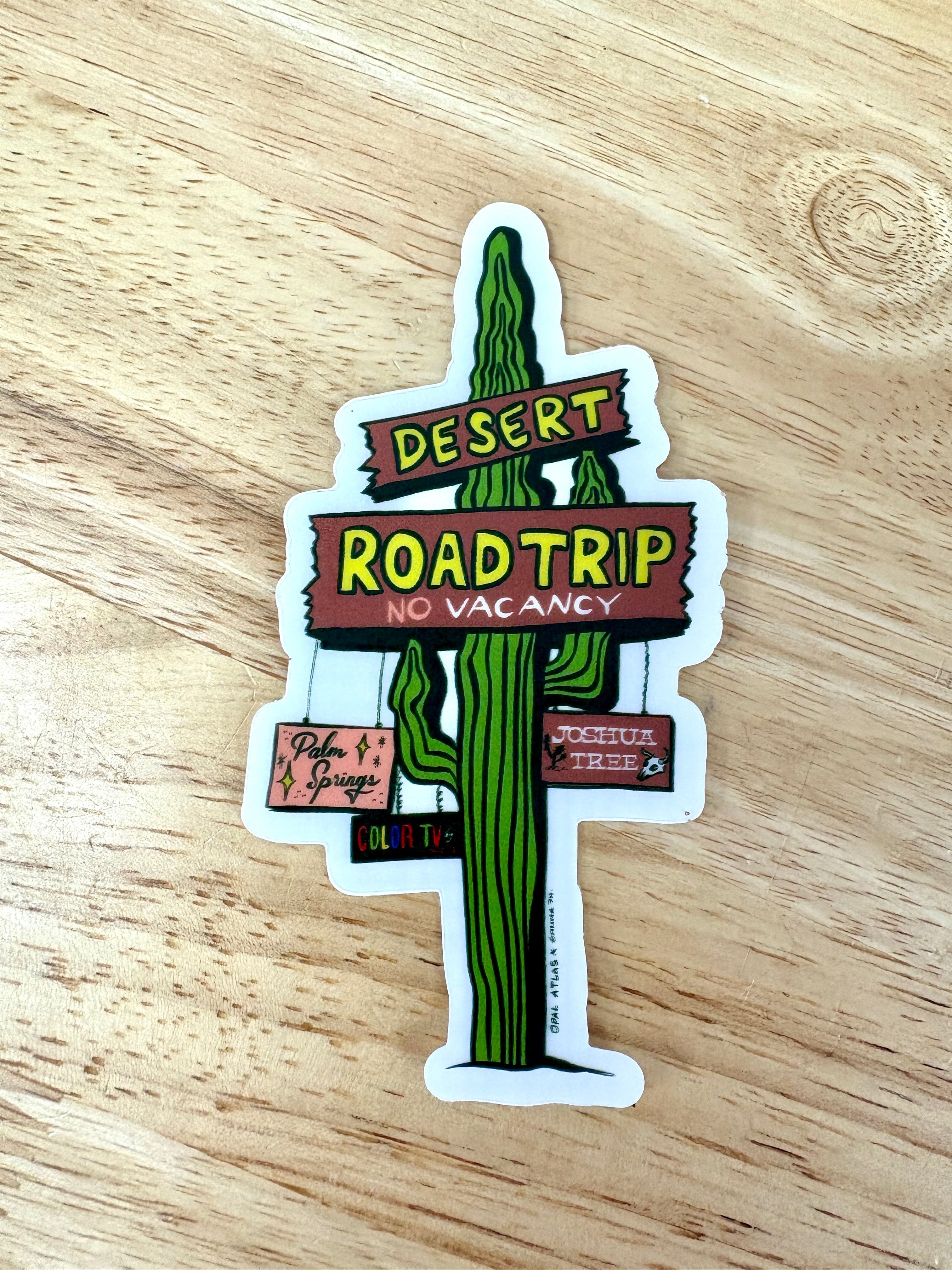 Sticker of a cactus with desert road trip text on a wooden surface