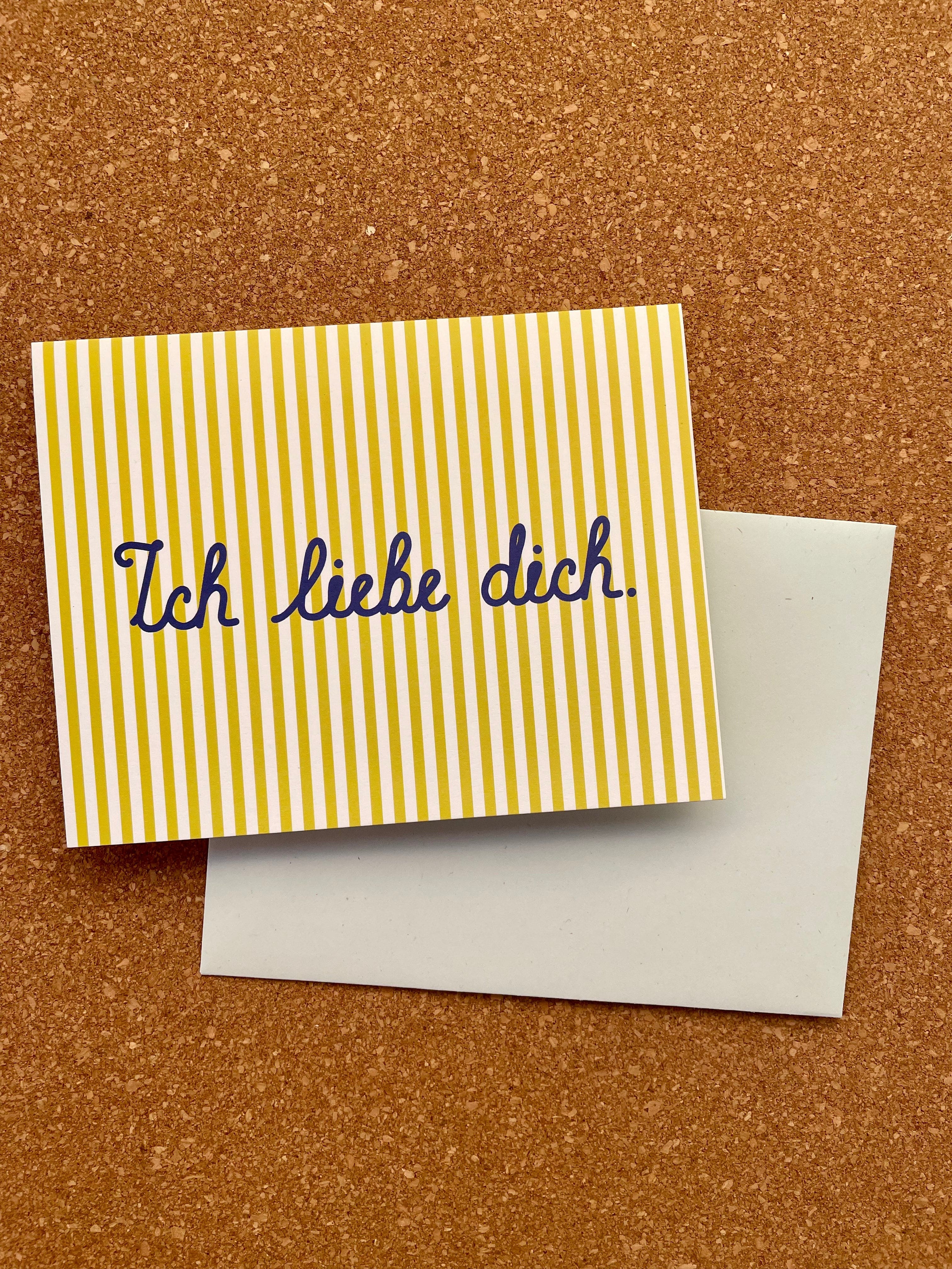 A bright yellow greeting card with the phrase 'Ich Liebe Dich' in blue script, paired with a pale blue envelope.