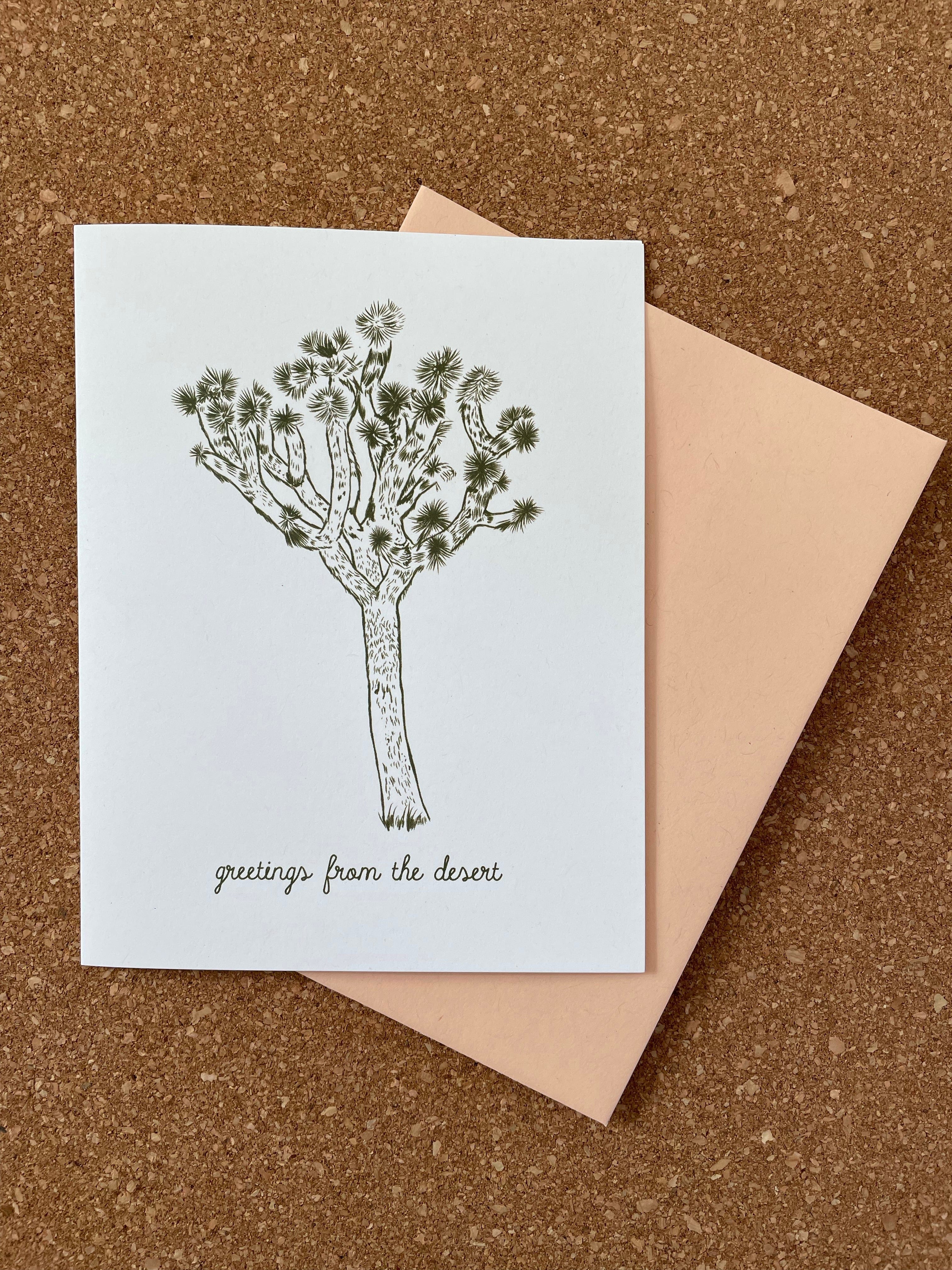 A greeting card featuring a green line drawing of a joshua tree on a white background, accompanied by an orange kraft-tone envelope.