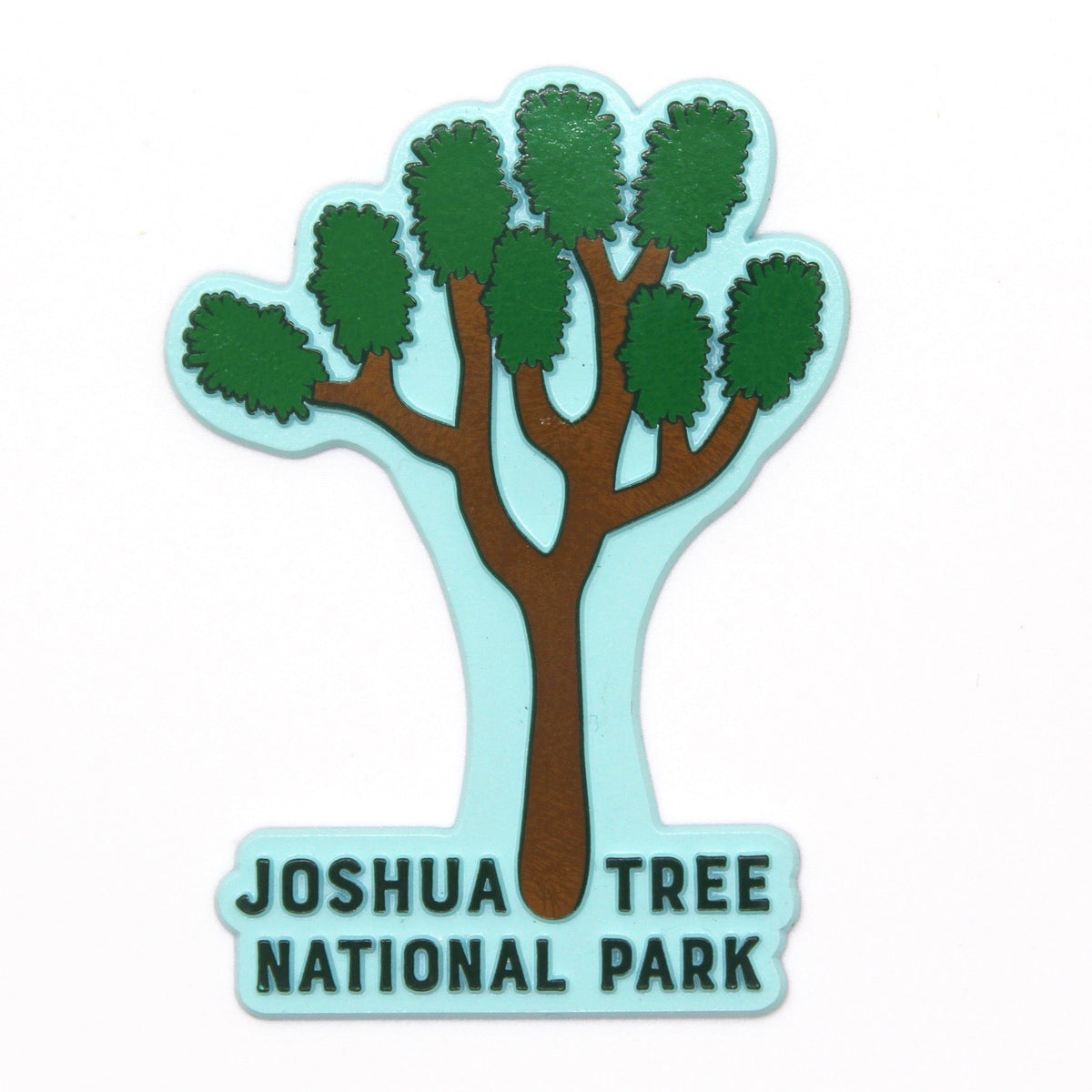 A rubber magnet with the shape of Joshua Tree National Park, featuring a stylized tree and text in green on a light blue background.