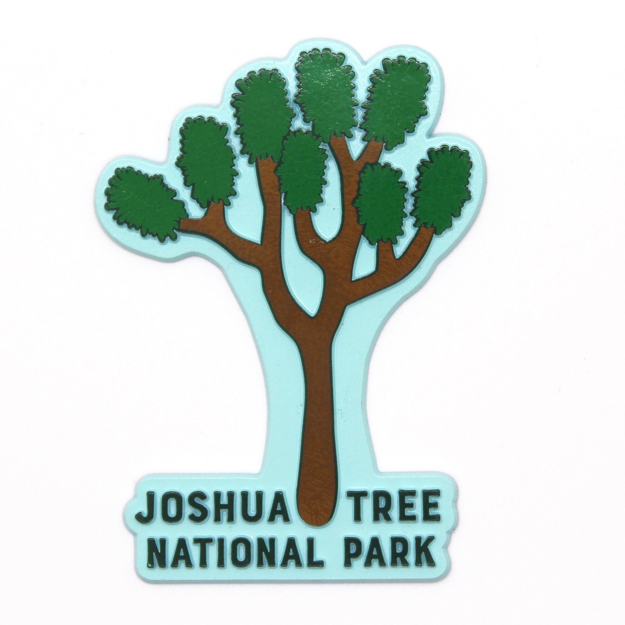 A rubber magnet with the shape of Joshua Tree National Park, featuring a stylized tree and text in green on a light blue background.