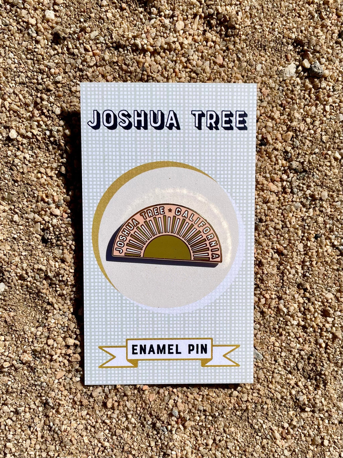 A gold and white enamel pin with the Joshua Tree design, displayed on a cardboard backing with the text 'JOSHUA TREE ENAMEL PIN'.