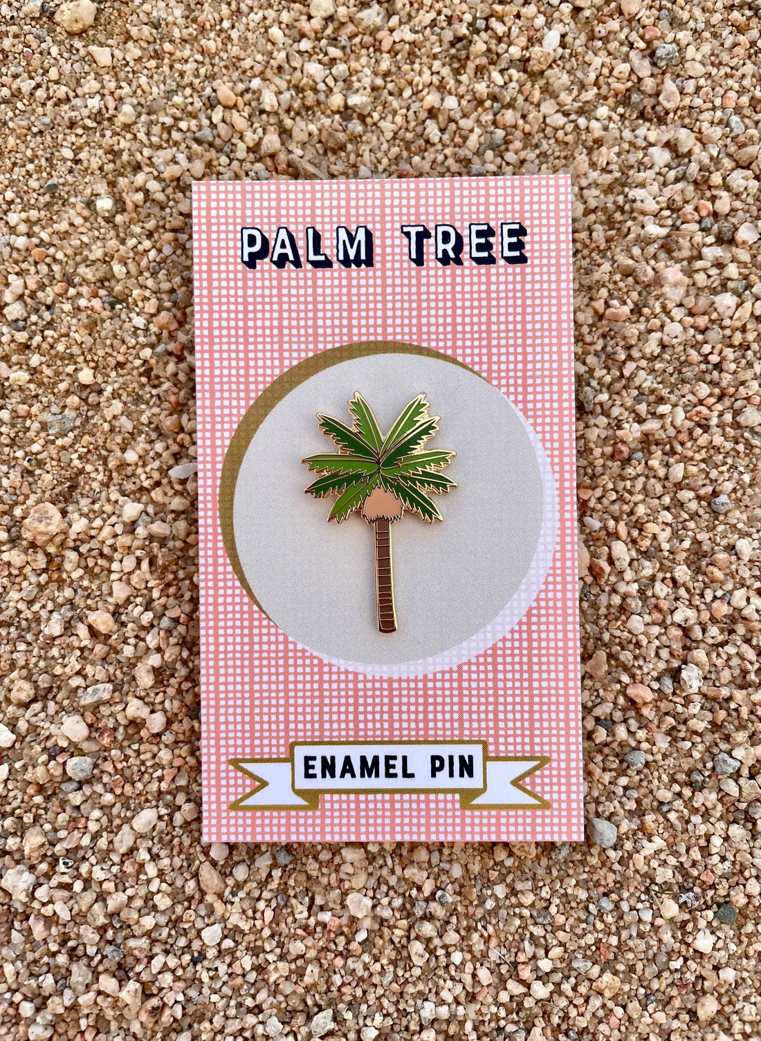 An enamel pin depicting a palm tree, displayed on a red and white checkered card with the text 'Palm Tree Enamel Pin'.