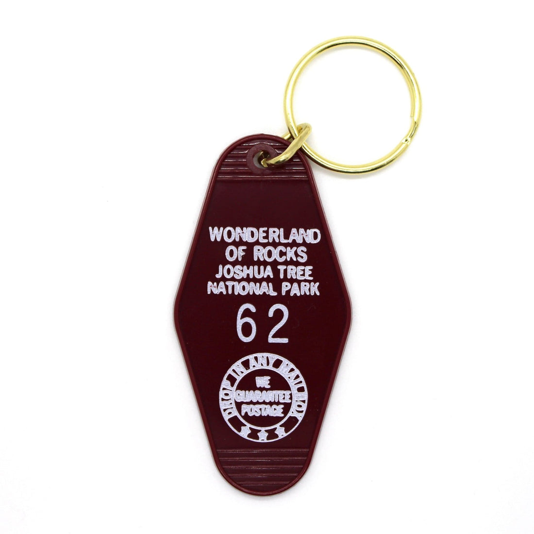 A dark red motel keychain with the text 'WONDERLAND JOSHUA TREE NATIONAL PARK 62' in white, attached to a brass keyring